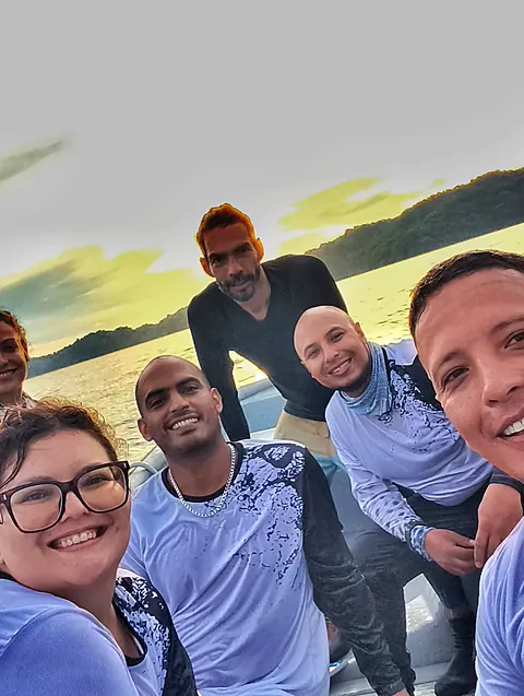 Selfie de seis makaras en la lancha al atardecer, con cerros verdes y el cielo dorado detrás
