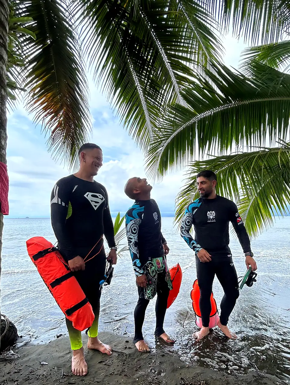 Tres apneístas con boyas rojas bajo palmeras a la orilla del mar
